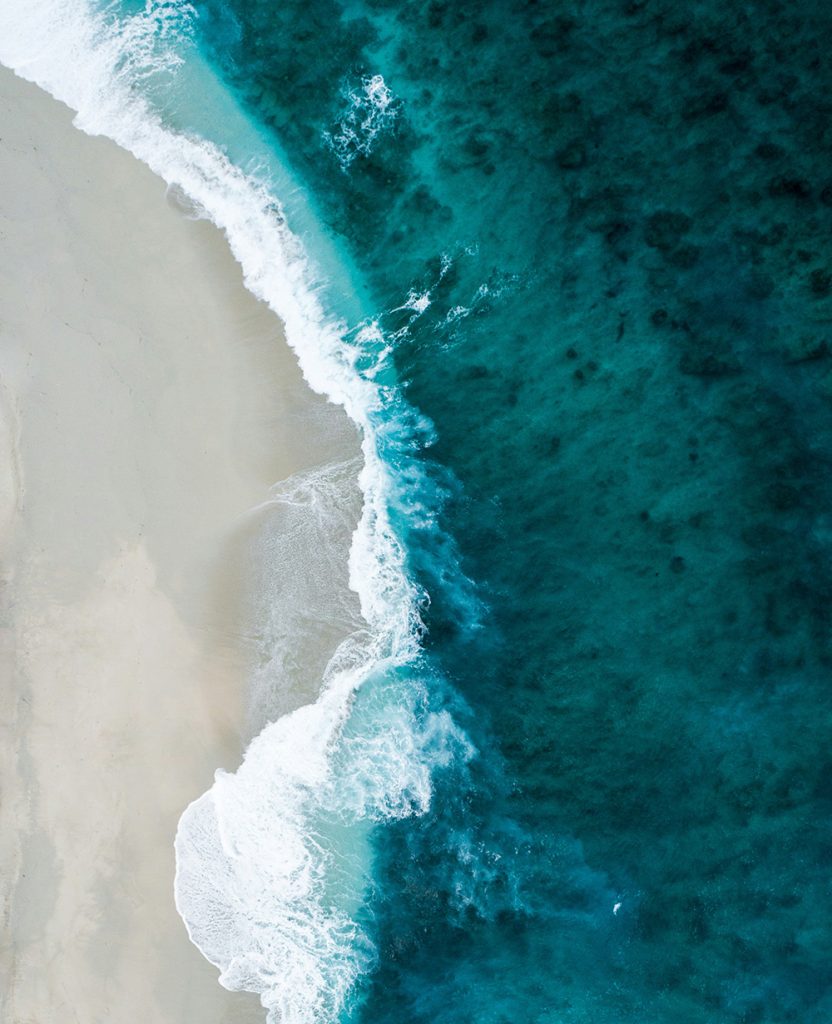 Aerial view of turquoise ocean waves gently crashing onto a white sandy beach, showcasing the contrast between sea and shore.