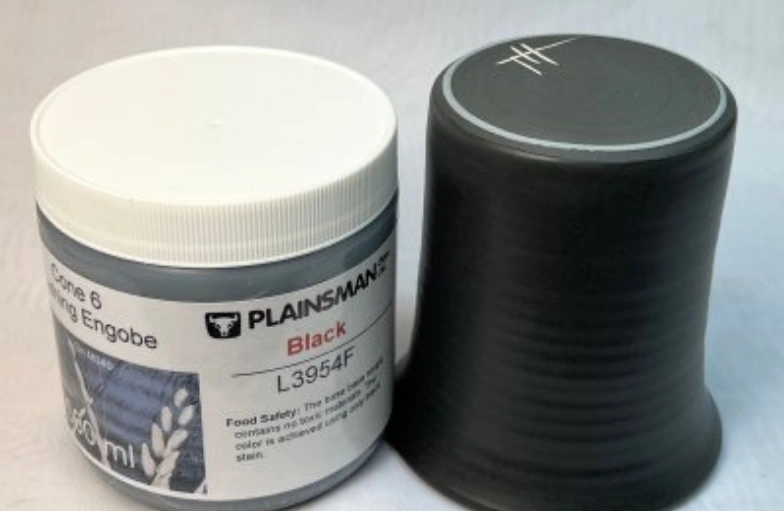 Jar of black Planamint Herbal Ointment next to a black silicone cupping therapy cup on a white surface.