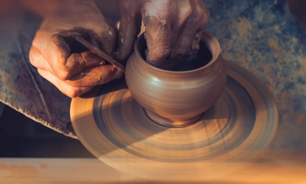 Close-up of hands shaping a clay pot on a spinning pottery wheel in a workshop.
