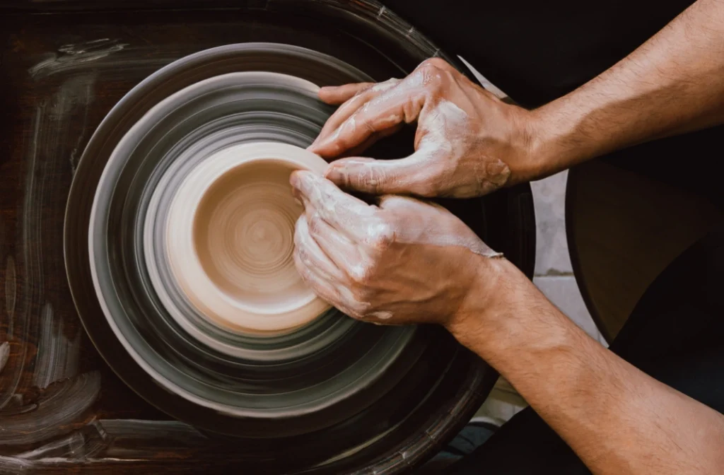 Hands shaping wet clay on a spinning pottery wheel, crafting a ceramic piece.