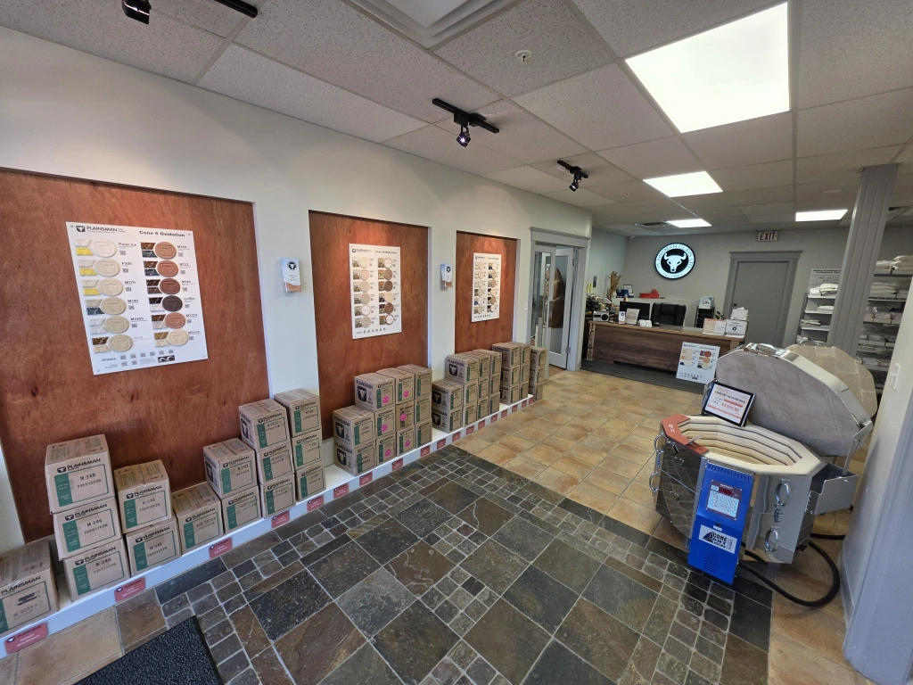 Interior view of a flooring showroom displaying tile samples on the walls and stacks of boxed tiles on the floor.