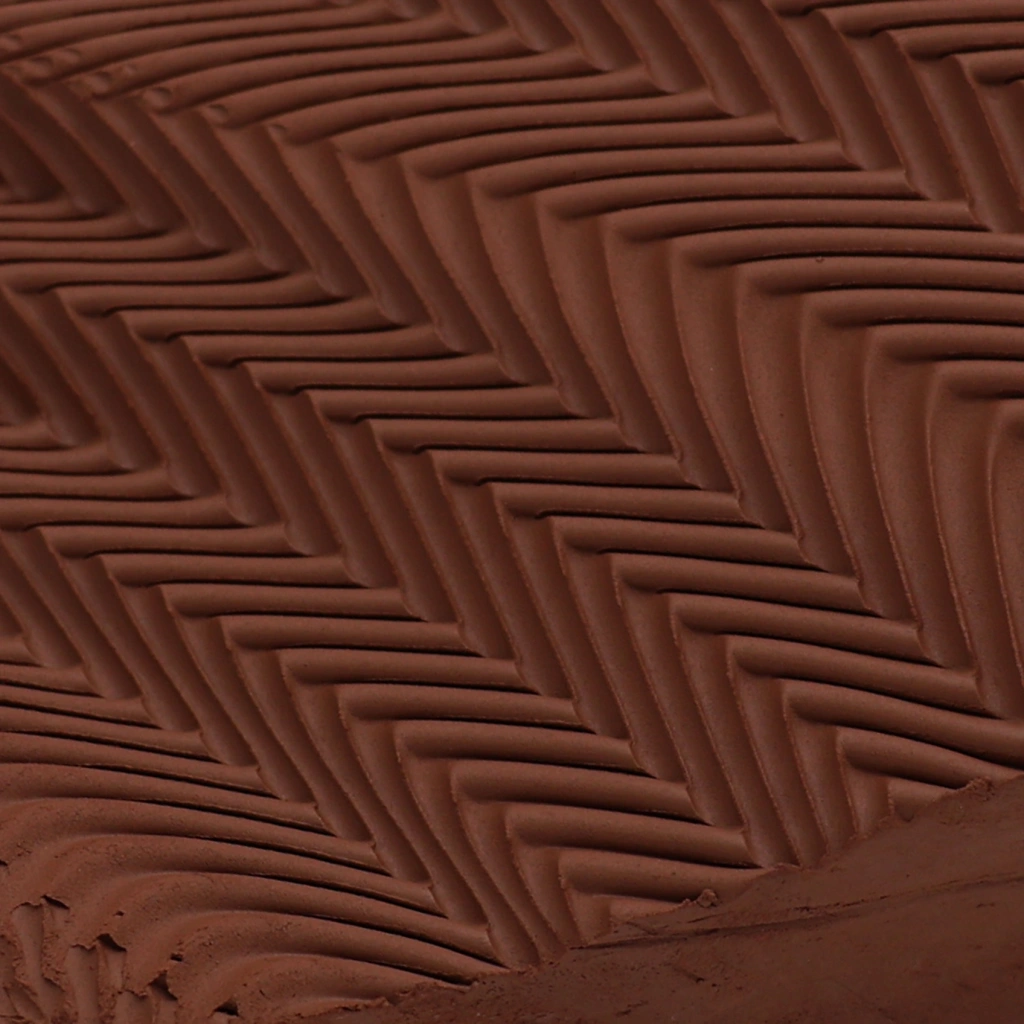 Close-up of dark brown clay with a textured herringbone pattern, showing detailed grooves and ridges.