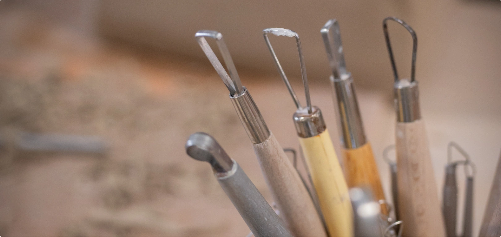 Close-up of various pottery sculpting tools with wooden and metal handles arranged in a container.