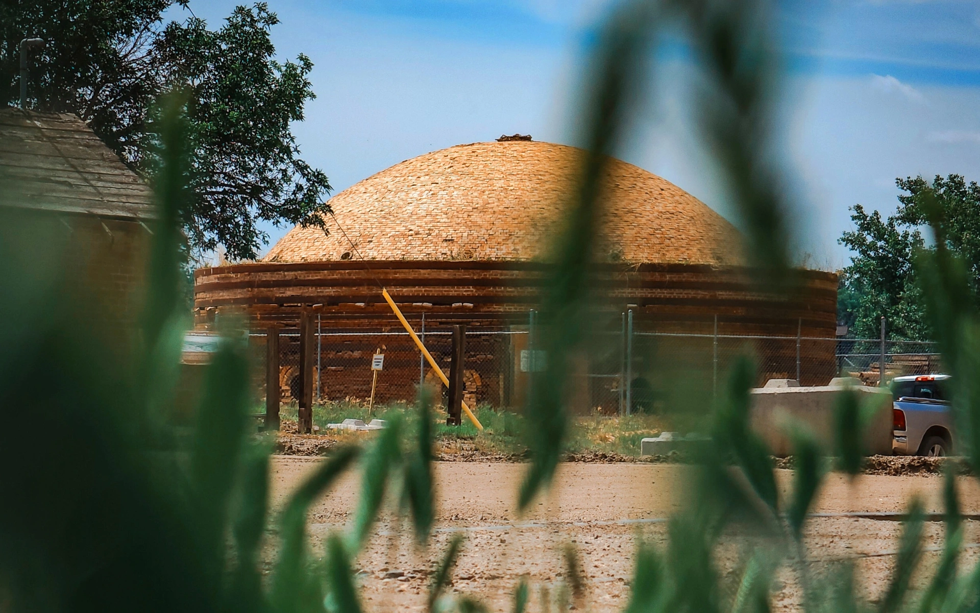 Round brick beehive kiln on the Plainsman site in Medicine Hat, seen through tall grass under a blue sky